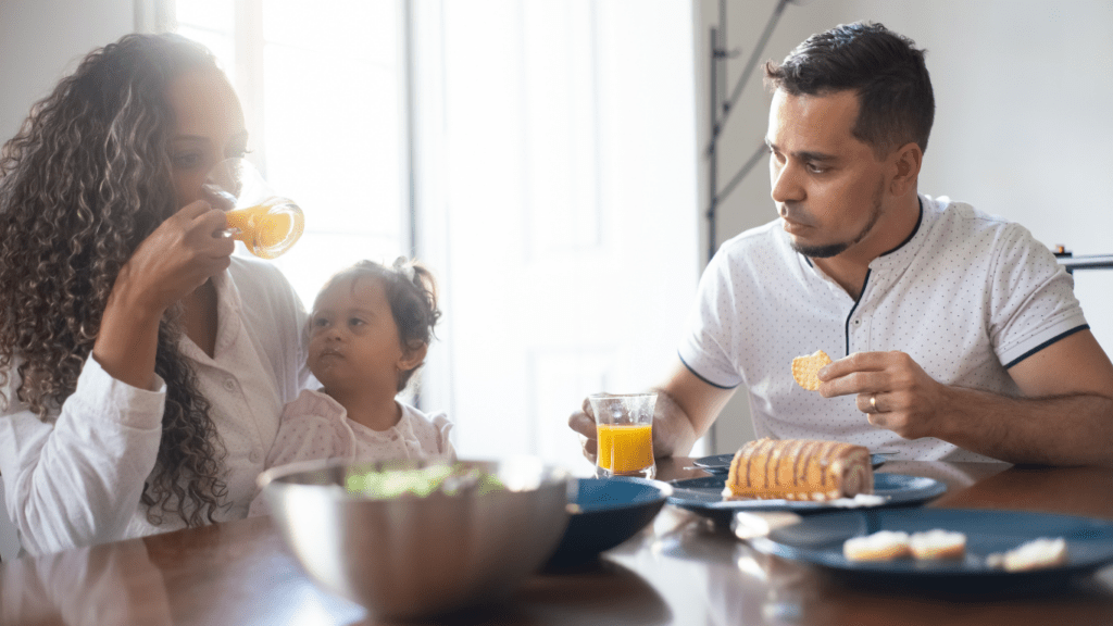 A parent and child are sitting at a table with a bowl of fruit and vegetables