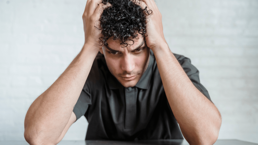 a person covers their face with their hands while sitting on a couch