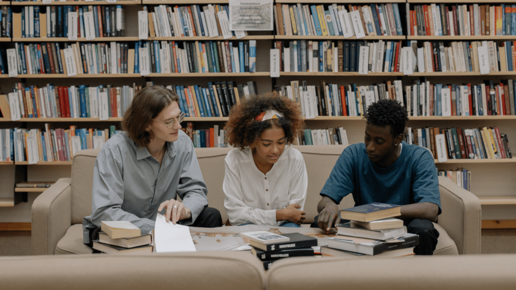 three students looking at a book in a library